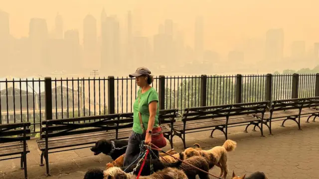 A dogwalker is seen passing the haze-obscured NYC skyline