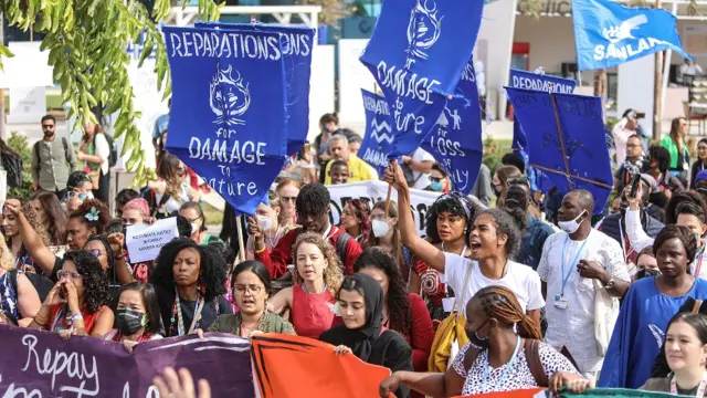Manifestantes con carteles que piden pagos por pérdidas y daños debidos al cambio climático