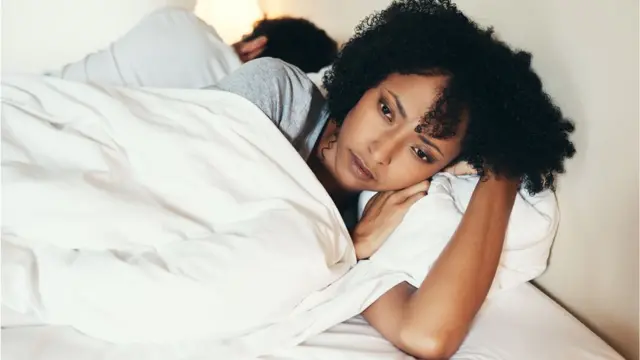 Une femme, le dos tourné à un homme, est pensive couchée sur son lit