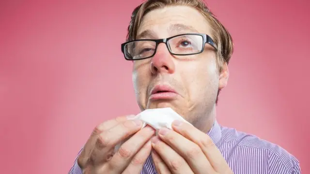 Una persona con cara de resfriado y un papel en la mano