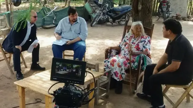 Uma senhora idosa dá depoimento para outros homens