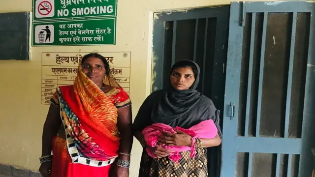 नवजात शिशु और अपनी माँ के साथ बिना मास्क के खड़ी मोहनपुरा गाँव की निवासी नीलम