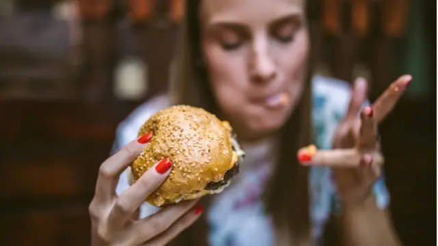 Una mujer comiendo una hamburguesa.