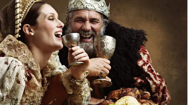 Мужчина и женщина в средневековых костюмах около блюда с виноградом, пирогами и жареной птицей