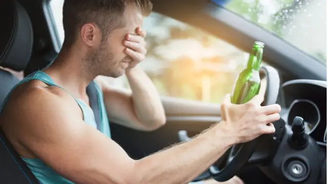 Hombre al volante con una botella en la mano