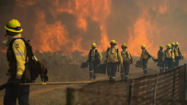 Firefighters leave one area wia di flames dey too aggressive, as di forest fire dey burn out of control on di foothills of Table Mountain