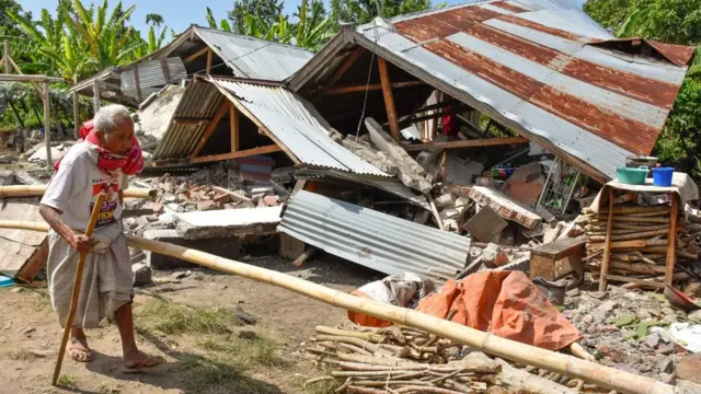 Warga berjalan di depan rumah yang roboh akibat gempa di Desa Sajang, Kecamatan Sembalun, Selong, Lombok Timur, NTB, Minggu (29/7).