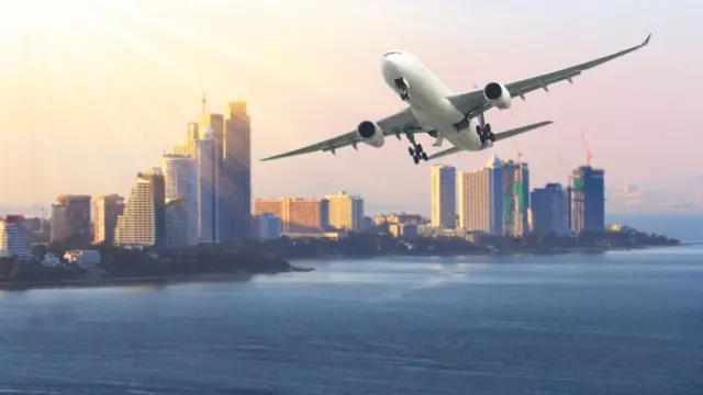 Un avión sobrevolando el mar. Al fondo una ciudad con rascacielos