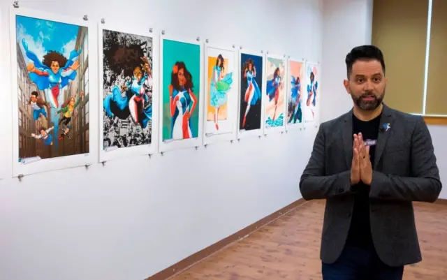 Edgardo Rodríguez-Miranda de pie junto a varios carteles con ilustraciones de La Borinqueña.