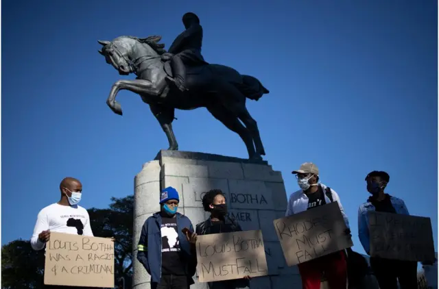 A nan masu zanga-zangar ne tsaye a kusa da mutum-mutumin Louis Botha a kan doki Firaminista na farko na Tarayyar Afirka ta Kudu inda suke neman a cire mutum-mutumin a gaban majalisar Afirka ta Kudu dake birnin Cape Town a ranar 16 ga Yuni 2020.