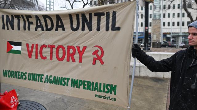 ناشط في كندا يحمل لافتة كتب عليها "الانتفاضة حتى النصر".