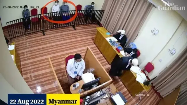 ဂါးဒီးယန်းက ဖော်ပြခဲ့တဲ့ ဒေါ်အောင်ဆန်းစုကြည်ရဲ့ တရားခွင် စီစီတီဗီပါ။ အဖြူရောင်အပေါ်ထပ်အင်္ကျီနဲ့ ဒေါ်အောင်ဆန်းစုကြည်ကထိုင်နေပြီး ရဲနှစ်ဦးက စောင့်ကြပ်နေပါတယ်။ တရားခွင်မှာ ရှေ့နေတစ်ဦးက တရားသူကြီးကို အမှုအကြောင်းရှင်းလင်းနေပါတယ်။