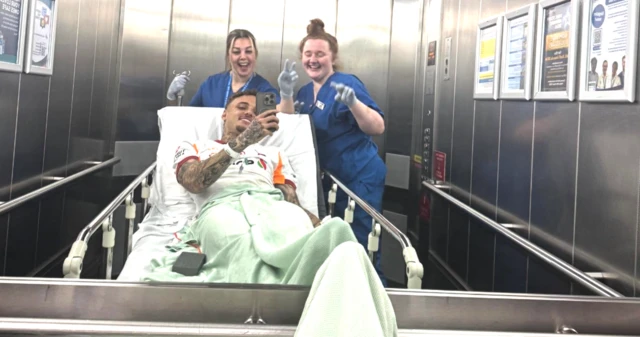 Noa Lang sedyde yatıyor, asansör aynasından kendisi ve ona refakat eden hemşireleri fotoğraflıyor.