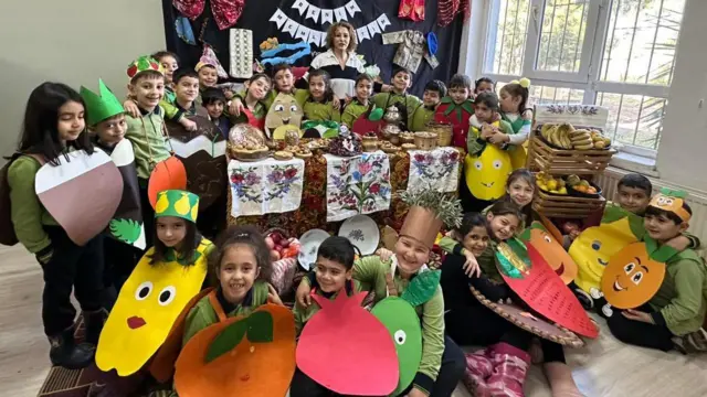 Sevgi Demir öğrencileri ile birlikte poz veriyor. öğrencilerin üzerinde farklı meyve kostümleri var.