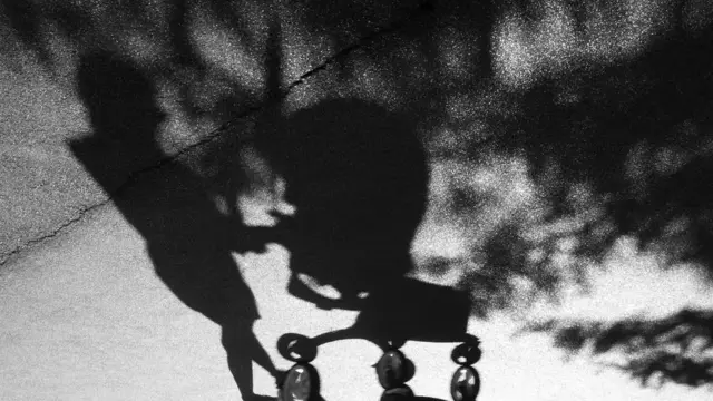 La sombra de una mujer empujando un coche de bebés.