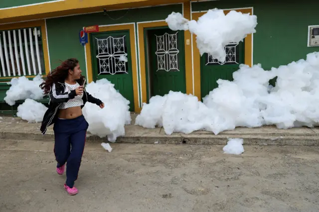 A woman flees from foam generated by a river full of waste, in a street in Mosquera, Colombia, April 27, 2022