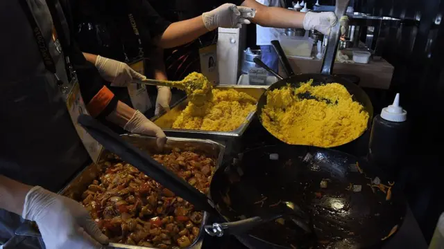 cocineros mueven con un cucharón dos recipientes con comida peruana.