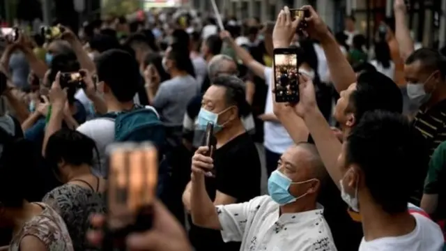 স্থানীয় মানুষজন কনস্যুলেটের বাইরে জড়ো হয়ে চীনের পতাকা নাড়াচ্ছেন এবং সেলফি তুলছেন।