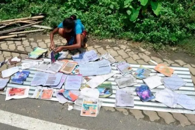 நீர் நனைந்த புத்தகத்தை வெயிலில் காய வைக்கும் பெண்