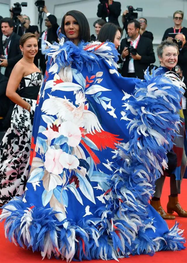 Iman wears a flamboyant dress featuring a red, white and blue pattern and feathers.