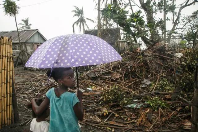 Deux petits enfants regardent les restes d'un bâtiment, l'un tient un parapluie.