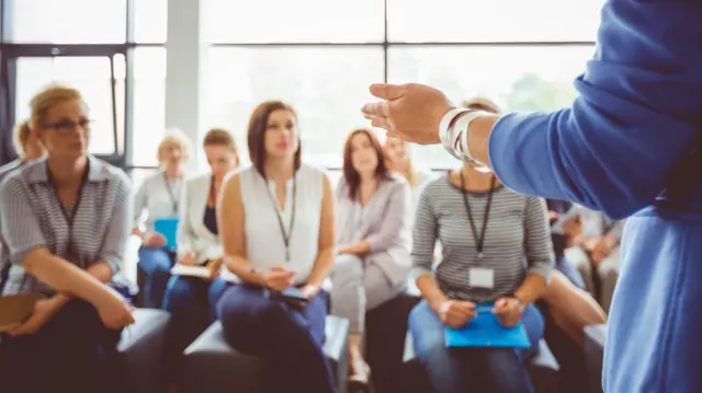 Mulhercomo jogar caca niqueiscostas falando para audiênciacomo jogar caca niqueismulheres sentadas e com crachás no pescoço