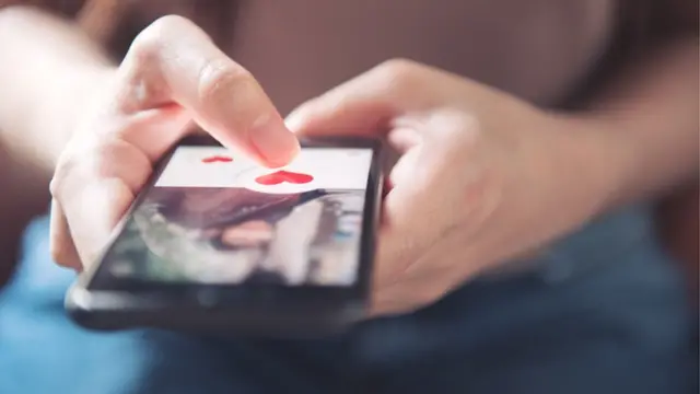 Una mujer sostiene un teléfono y le da me gusta a una foto.