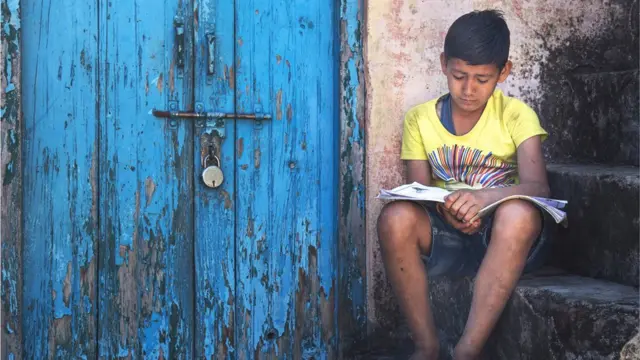 Menino lendo com semblante infeliz, ao ladoxxxtreme roletauma porta azul trancada a cadeado