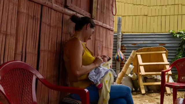 Una mujer de camiseta amarilla con un bebé en brazos