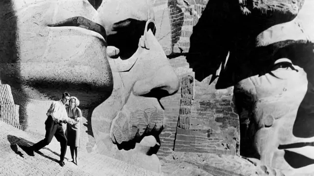 Герои фильма Альфреда Хичкока «К северу через северо-запад» Роджер Торнхилл (Кэри Грант) и Ив Кендал (Эва Мари Сент) прячутся от своих преследователей среди огромных голов президентов на горе Рашмор