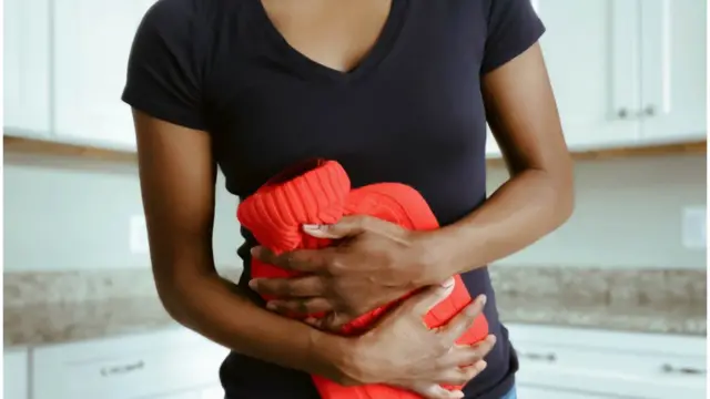 Foto mostra mulher com cólica usando bolsabetbrasil365água quente no abdômen