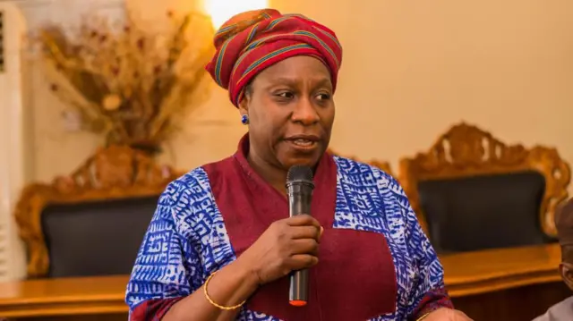 Senetor Iyabo Obasanjo-Bello. O we gele alawọ pupa, wọ aṣọ alawọ aro. O mu ẹrọ gbohun-gbohun dani bo ṣe n sọrọ.