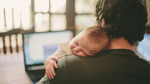 Un padre carga a un bebé mientras trabaja.