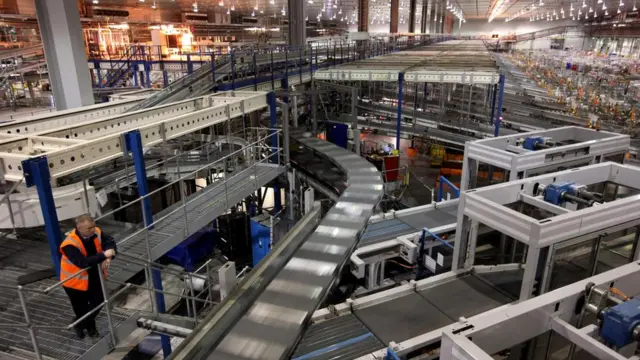 Один-единственный работник наблюдает за работой автоматического сортировочного оборудования на складе супермаркета Sainsbury's