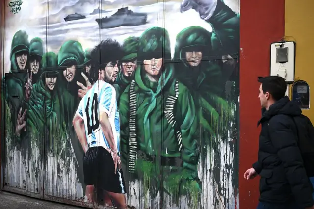 14 Temmuz 2026'da Buenos Aires'te, Arjantinli futbol efsanesi Diego Maradona ile Falkland Savaşı'nda görev yapan Arjantinli askerleri tasvir eden bir duvar resminin önünden bir kişi geçiyor.