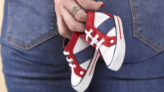 Mujer con unos zapatos de bebé a su espalda.