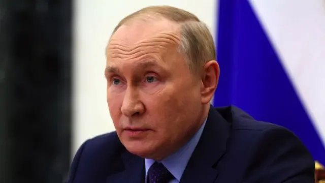 Vladimir Putin sits in front of a Russian flag.