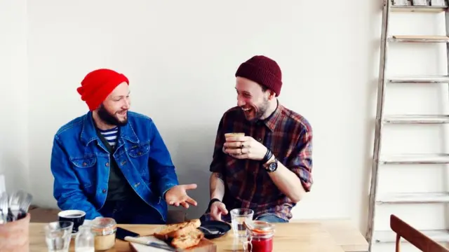 Dos personas trabajando en una casa, al parecer en decoración de interiores, durante una pausa, comiendo