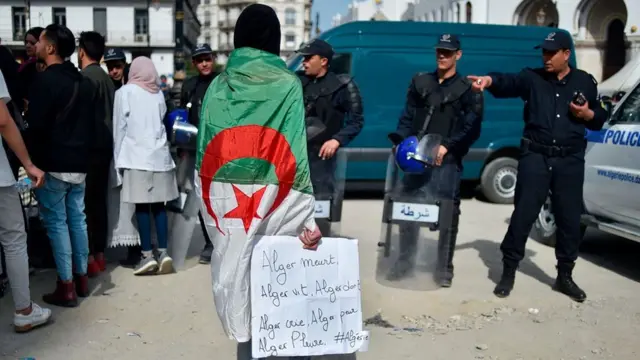 A young man, wearing the national flag, holds a banner as Algerian students demonstrate in the capital Algiers on March 5, 2019