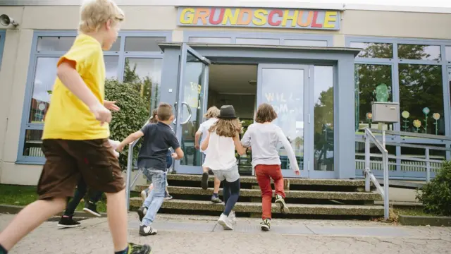 Crianças correm para entrarestratégia para roleta cassinoum edifício, onde está escrito 'Grundschule' (escola primária,estratégia para roleta cassinoalemão)