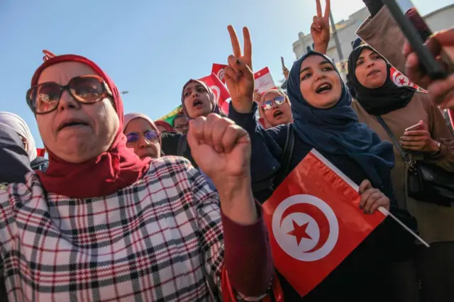 Female demonstrators make the victory sign (V sign) as they shout slogans while holding Tunisian flags, during a demonstration called by the protest movement known as Citizens Against Coup, held near the building of the Tunisian Parliament in the city of Bardo, in Tunis, Tunisia, on November 14, 2021