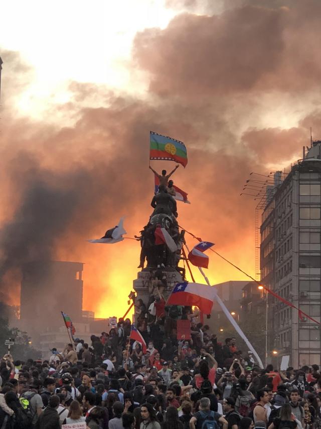 La imagen de un manifestante flameando la bandera mapuche en la cima de una estatua militar, en Santiago