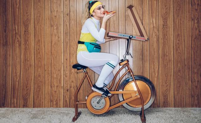 Mujer en bicicleta de ejercicio comiendo pizza