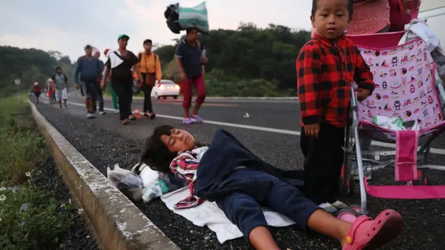 Una niña duerme sobre el pavimento mientras detrás de ella caminan migrantes provenientes de Centroamérica.