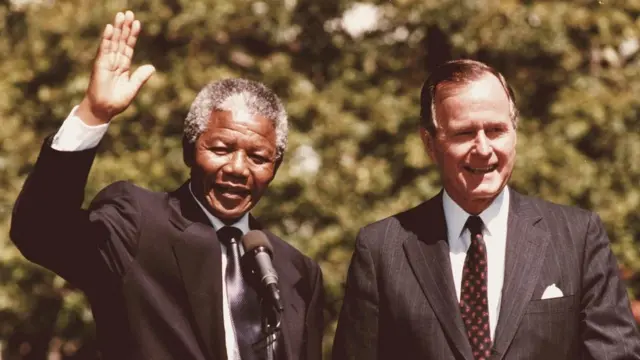 June 24, 1990 shows South African anti-apartheid leader and African National Congress (ANC) member Nelson Mandela (L) waves to the media and fans after finishing his joint statement with former US President George Bush (R) on the White House South Lawn in Washington,DC