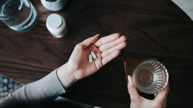 Mulher segura comprimidoscasino bruma mão e copocasino brágua na outra