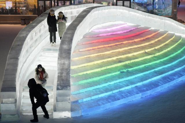People walk on an ice bridge lit up in rainbow colours