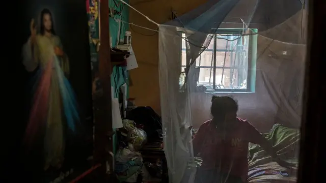 Una mujer sentada en su cama alrededor de la cual colocó una red contra mosquitos