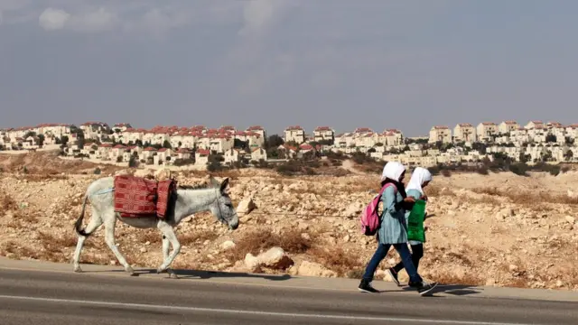 Niñas palestinas caminan un burro. En el fondo, un asentamiento cisjordano de Maale Adumim