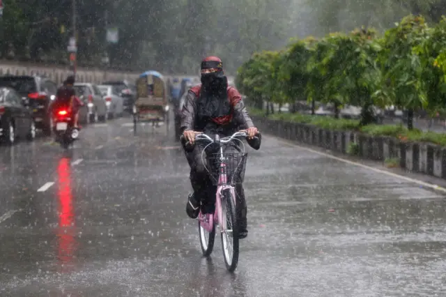 বৃষ্টিতে সাইকেল চালিয়ে যাচ্ছেন একজন নারী